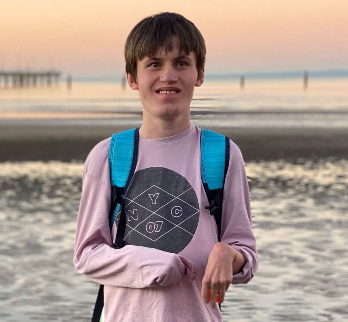 A boy who is an NDIS participant standing on the beach during sunset.